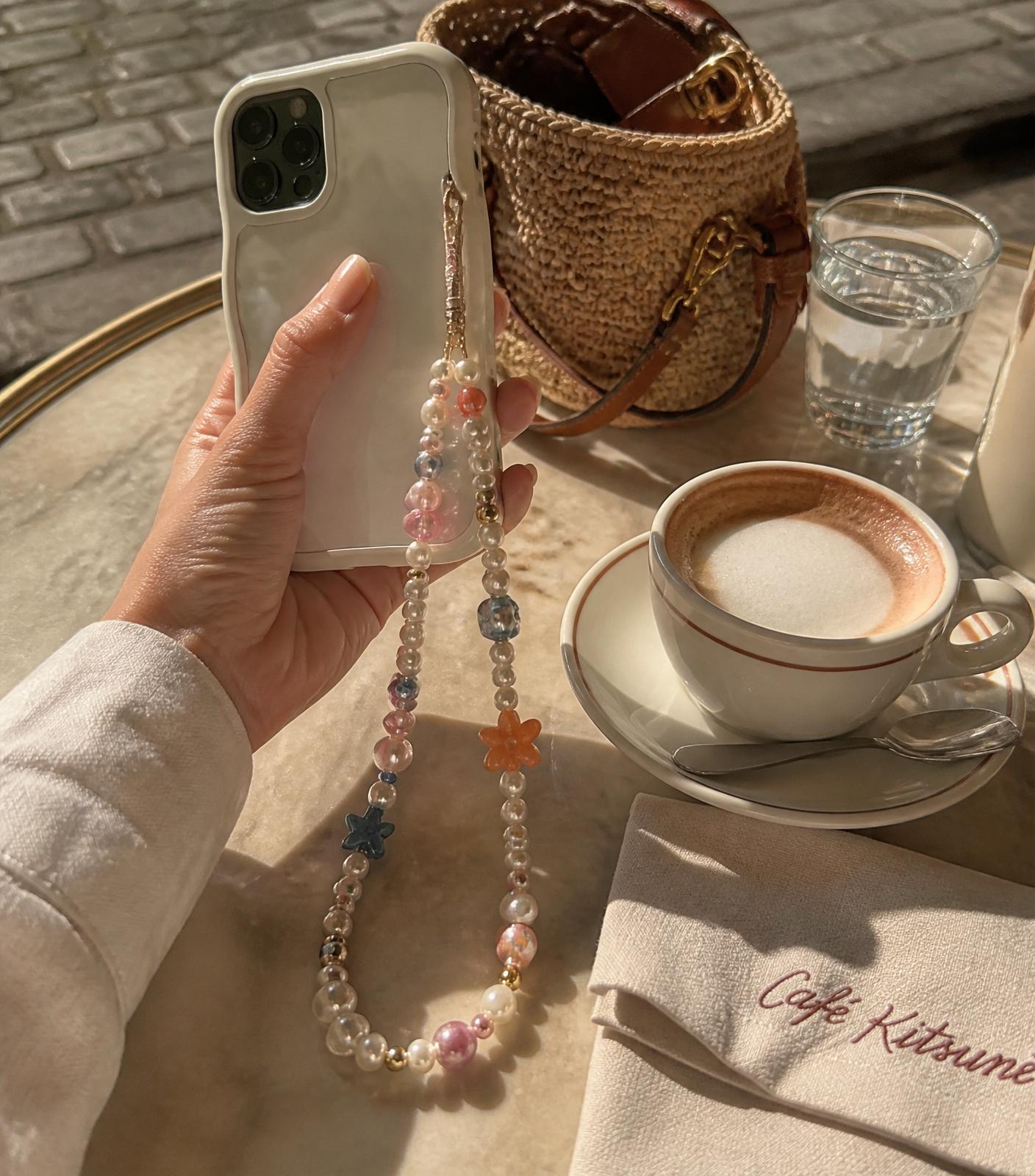 A colorful beaded phone chain on a phone at a Parisian cafe